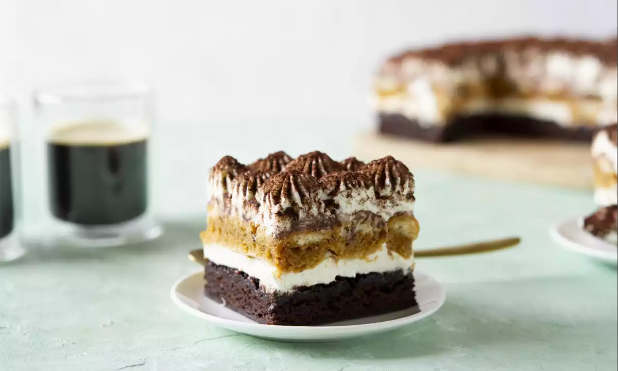 Brownie tiramisu with a dark chocolate brownie base, layers of whipped cream, coffee-soaked sponge, and cocoa-dusted cream on a white plate