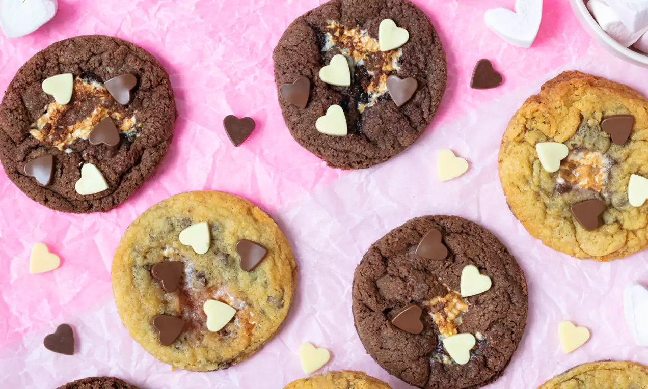Chocolate and golden cookies with heart-shaped chocolate pieces, soft marshmallow centers, arranged on crinkled pink paper
