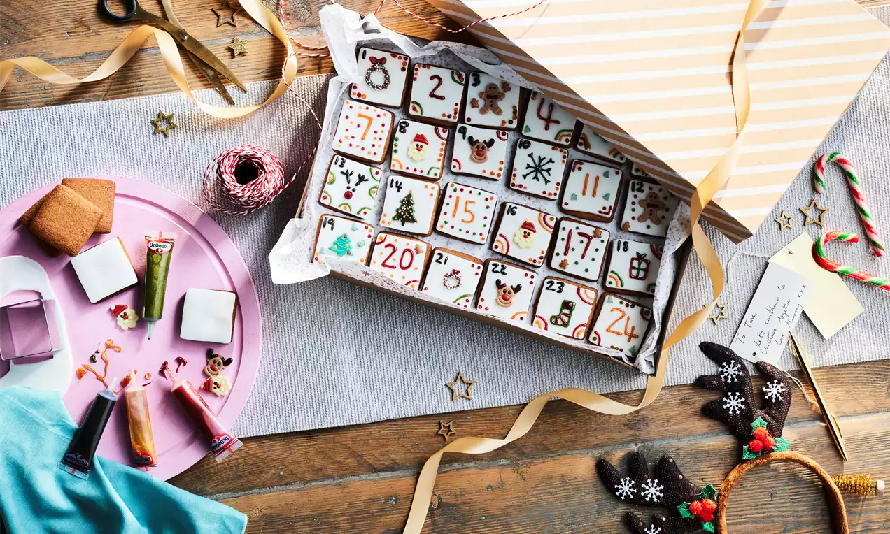 A festive Advent calendar with intricately painted numbered chocolate squares in a striped box surrounded by holiday decorations