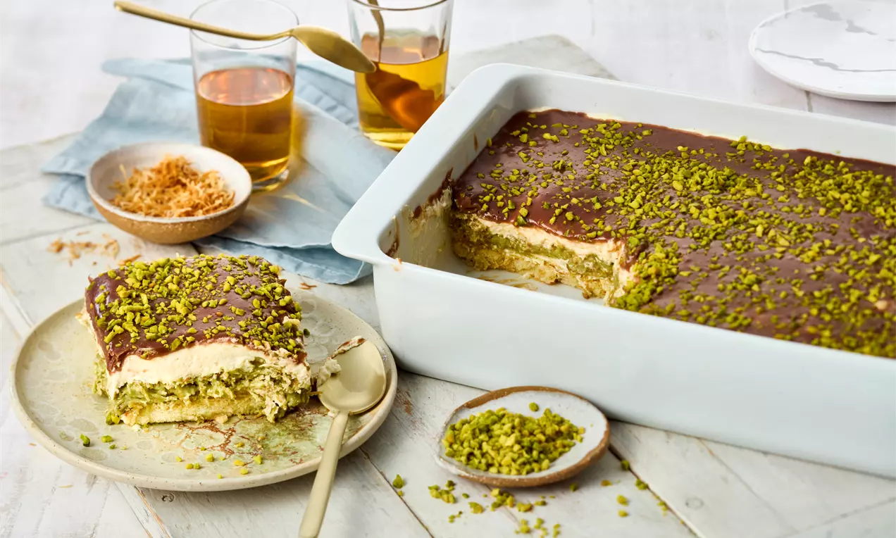 Dubai Chocolate Tiramisu with rich cocoa glaze, creamy layers, and vibrant pistachio pieces in a white dish and on a beige plate